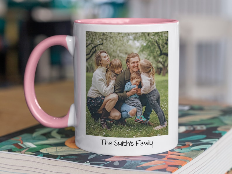 Puede incluir: Una taza de cer&aacute;mica blanca con un borde y un asa de color rosa. La taza presenta una foto de una familia de cuatro personas en un entorno de jard&iacute;n. El texto "The Smith's Family" est&aacute; impreso en la parte inferior de la taza.