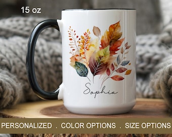 May include: White ceramic mug with a black handle. The mug features a watercolor design of autumn leaves in shades of orange, yellow, red, and green. The name "Sophia" is written in cursive at the bottom of the mug. The mug is 15 ounces.