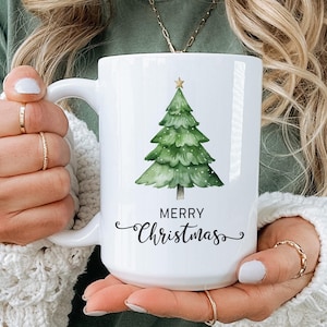 May include: White ceramic mug with a green watercolor Christmas tree and the text "Merry Christmas".