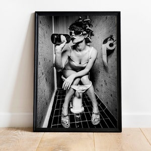 Può includere: Foto in bianco e nero di una persona seduta su un water in un bagno, con occhiali da sole e che beve da una bottiglia.