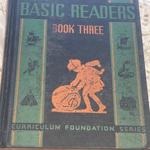 May include: A vintage book titled "Basic Readers Book Three" by Elson-Gray. The cover features a green and black color scheme with illustrations of a ship, a Native American, a teepee, a snake, and two children rolling a ball. The book is part of the "Curriculum Foundation Series".