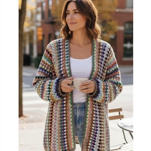 May include: A long, open-front crochet cardigan in a patchwork design. The sweater features a mix of colors including brown, blue, green, and pink. The sleeves are long, and the cardigan is worn over a white top and blue jeans.