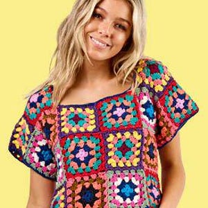 May include: A colorful crochet top with a square neckline. The top features a patchwork design with various colors including red, blue, yellow, and green. The short-sleeved top is made of yarn and is worn with blue jeans.