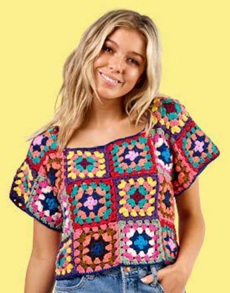 May include: A colorful crochet top with a square neckline. The top features a patchwork design with various colors including red, blue, yellow, and green. The short-sleeved top is made of yarn and is worn with blue jeans.