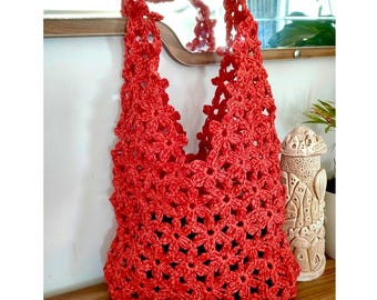 May include: A vibrant red crochet tote bag, featuring a floral pattern. The bag has a handle made of the same crochet material and design. The bag is displayed on a wooden surface.
