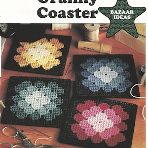 May include: Four crocheted granny square coasters in different colour combinations: yellow, white, and brown; blue, white, and black; teal, white, and black; and pink, white, and red. The coasters are on a wooden surface with sewing supplies.