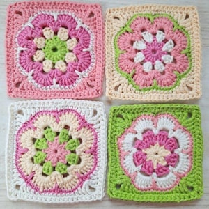 Könnte beinhalten: Vier quadratische Häkelstücke mit Blumenmustern. Jedes Stück zeigt ein Blumenmuster in Rosa, Grün, Weiß und Creme. Die handgefertigten Quadrate sind zusammen angeordnet und zeigen die Details und Farbkombinationen.
