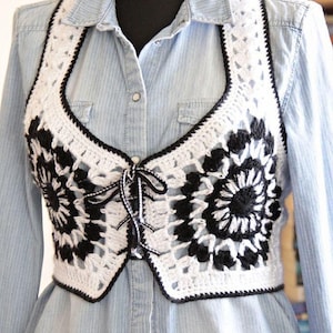 May include: A black and white crocheted vest with a lace-up front. The vest is made of granny squares with a black and white floral design.