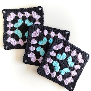 Puede incluir: Tres cuadrados de ganchillo en negro, lavanda y turquesa. Los cuadrados están hechos con un patrón de punto de granny.