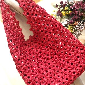 May include: A handmade red crochet tote bag with a floral pattern. The bag features a sturdy handle and a spacious interior. The crochet design is intricate, with a repeating flower motif. The bag is made of a soft, durable material, perfect for carrying everyday items.