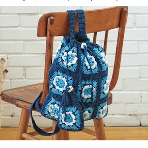 May include: A handmade crochet backpack in shades of blue and white, with a floral square pattern. The drawstring bag hangs on a wooden chair. The bag has a matching small pouch.