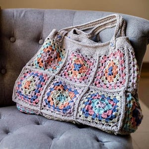 Könnte beinhalten: Eine gehäkelte Tragetasche mit grauem Hintergrund und bunten Granny Squares. Die Tasche hat zwei Henkel und ist aus verschiedenen Pastellfarben gefertigt.