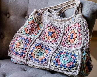 May include: A crocheted tote bag with a gray background and colorful granny squares. The bag has two straps and is made with a variety of pastel colors.