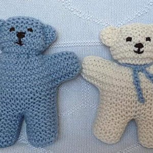Può includere: Due orsacchiotti di peluche a maglia, uno blu e uno bianco, con occhi e naso neri. L'orso bianco ha una sciarpa blu.