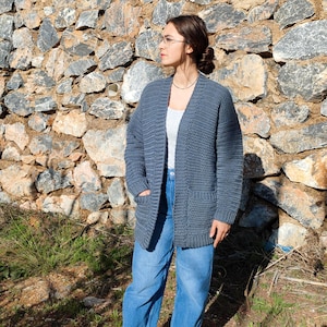 May include: A blue crocheted cardigan with a deep V-neck and two pockets. The cardigan is worn over a white t-shirt and blue jeans.