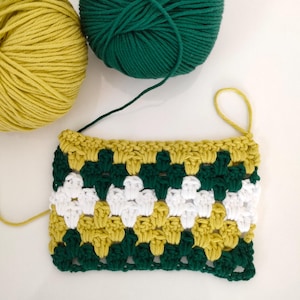 May include: A crochet square with a green, white, and yellow pattern. The square is made with different colored yarn.
