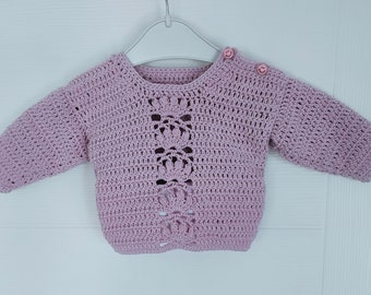 Puede incluir: Un suéter de punto de color lila claro con un delicado diseño calado y botones rosas.