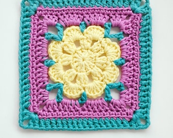 Puede incluir: Pieza cuadrada de ganchillo con una flor amarilla central, un borde morado y un borde turquesa. El artículo hecho a mano muestra puntadas detalladas y una combinación de colores vibrantes. Ideal para proyectos de artesanía o decoración del hogar.