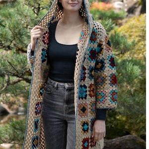 Könnte beinhalten: Ein gehäkelter Cardigan mit Kapuze, der ein farbenfrohes Patchwork-Design aus Quadraten in Blautönen, Rot, Gelb und Braun aufweist. Der Cardigan ist aus beigefarbenem Garn gefertigt und hat einen blauen Saum.