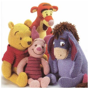 May include: A group of four crocheted plush toys featuring characters from Winnie the Pooh. The toys include Winnie the Pooh in yellow, Tigger in orange, Piglet in pink, and Eeyore in blue. Each toy has detailed facial features.