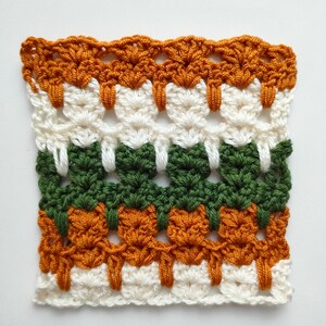 May include: A crocheted square with a repeating pattern in orange, white, and green yarn.