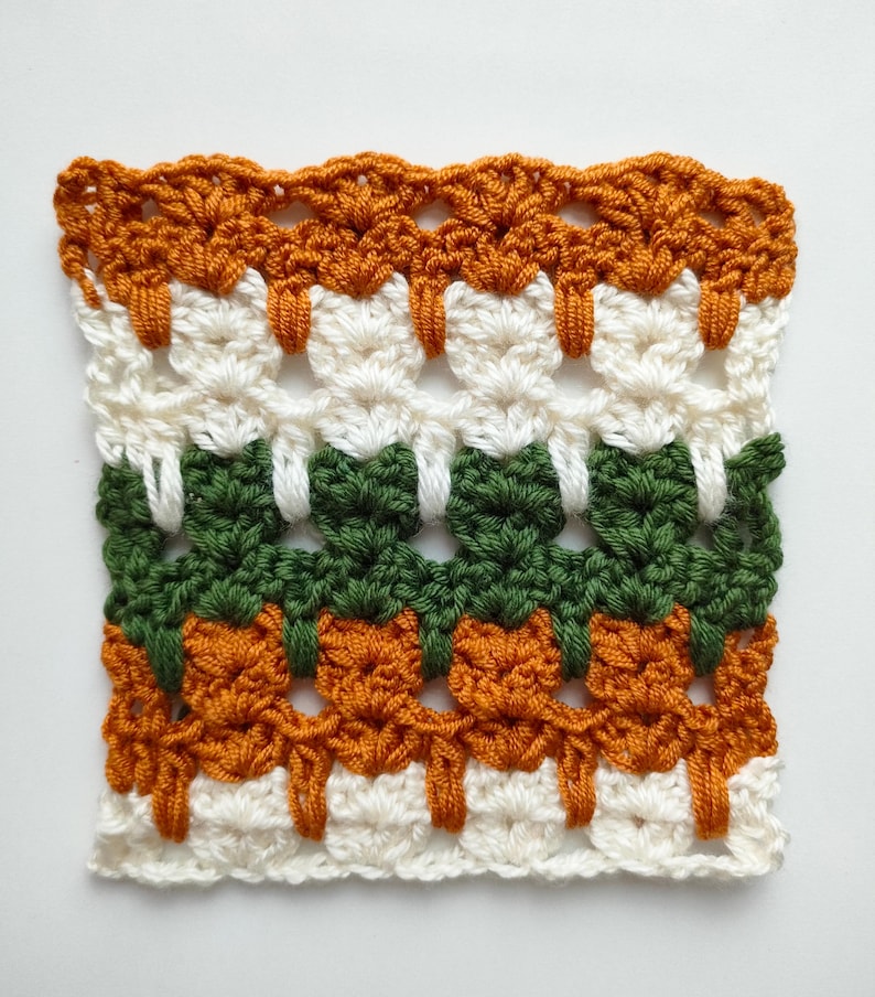 May include: A crocheted square with a repeating pattern in orange, white, and green yarn.
