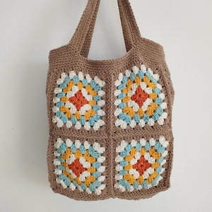 May include: A brown crocheted tote bag with four colorful granny squares. The squares are made with white, orange, yellow, and blue yarn.
