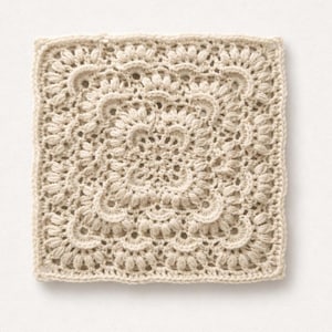 May include: A square, cream-coloured crochet piece with a detailed floral pattern. The design features multiple layers of textured stitches, creating a raised, dimensional effect. The edges are neatly finished, showcasing the intricate craftsmanship.