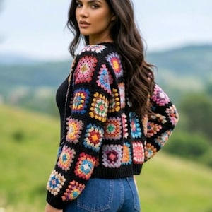 Puede incluir: Un cárdigan de manga larga confeccionado con hilo negro que presenta un patrón de cuadrados de la abuela multicolor. La prenda tiene cuello redondo, puños acanalados y dobladillo acanalado, mostrando una vibrante gama de cuadrados rosas, azules, amarillos y rojos.
