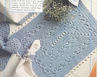 Op de afbeelding: Een vierkant placemat van blauw gehaakt materiaal met een witte gehaakte rand. De placemat is gemaakt met een delicaat steekpatroon en heeft een servetring erop.