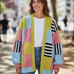 May include: A patchwork cardigan in pastel colors, including pink, blue, and yellow, with black and white striped accents on the sleeves. The open-front sweater is worn over a white top and blue jeans.