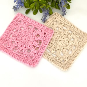 May include: Two square crochet coasters. One is light pink, the other is beige. Each coaster features a floral design in the center and a solid border. The coasters are handmade and suitable for home decor.