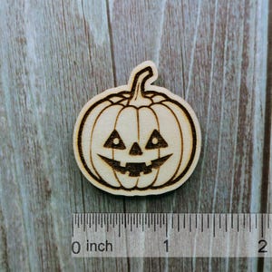Könnte beinhalten: Ein hölzerner Kürbis mit einem geschnitzten Jack-o'-Lantern-Gesicht. Der Kürbis hat einen Durchmesser von etwa 2,5 cm.