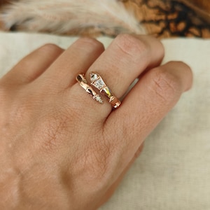 Könnte beinhalten: Roségoldener Ring mit Bambus-Design. Der Ring hat einen Wickelstil mit einer Ansammlung klarer Kristalle auf der Oberseite. Der Ring befindet sich an einer Hand.