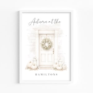 May include: A framed wall art print featuring a watercolour illustration of a white front door with a wreath, lanterns, and pumpkins. The text reads Autumn at the HAMILTONS in black script and block lettering against a neutral background.