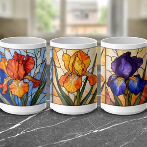 May include: Three white ceramic mugs with a stained glass design of iris flowers. The mugs feature different colored irises: orange, yellow, and purple.