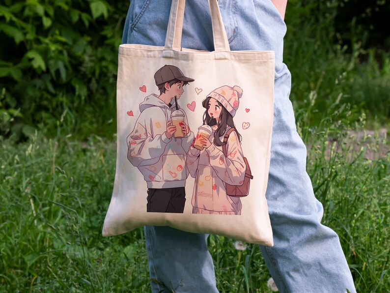 May include: A white canvas tote bag with a printed design of two cartoon characters holding beverages. The characters are a man with a black hoodie and a woman with a pink hoodie. The design includes pink hearts and other small details.
