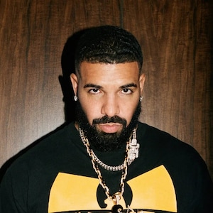 May include: A man with a short beard and black hair is wearing a black t-shirt with a yellow Wu-Tang Clan logo. He is wearing a gold chain with a diamond pendant.