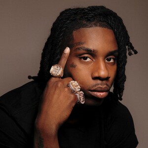 May include: A person wearing multiple gold rings with intricate designs. The person is also wearing a black shirt. The person has a tattoo on their forehead that says "TORN".