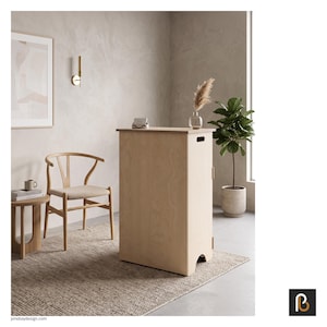 May include: A tall, rectangular light-coloured wooden cabinet with a smooth finish, featuring a cutout handle near the top edge and a curved base opening. The cabinet stands upright on a textured rug, showcasing a simple, functional design.