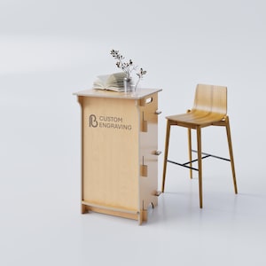 May include: A light wood-toned bar with the text "CUSTOM ENGRAVING" and a matching bar stool. The bar has a small countertop with a book and a vase of greenery. The stool has a curved seat and black metal supports.