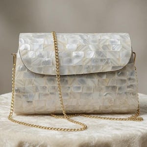 May include: A rectangular clutch bag featuring a mosaic of iridescent white mother-of-pearl tiles across the exterior surface. The bag includes a gold-toned metal chain shoulder strap attached to the sides and a flap closure on the front.