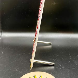 May include: A white picture frame with a red and white design. The frame is standing on a small metal stand. The frame is decorated with rhinestones. The frame is sitting on a brown coaster with a yellow sun and moon design and the text "Creations by Day".