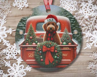 May include: A red vintage truck with a Christmas wreath and ornaments in the bed. A brown dog wearing a red Santa hat with the name "Lola" on it is sitting in the truck bed. The truck has the text "2024" on each side of the bed.