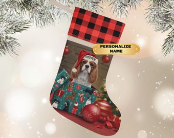 May include: A Christmas stocking with a red and black buffalo plaid cuff. The stocking features a Cavalier King Charles Spaniel wearing a Santa hat with the name "Cooper". The stocking is decorated with gift boxes and ornaments. The text "PERSONALIZE NAME" is on a gold banner.