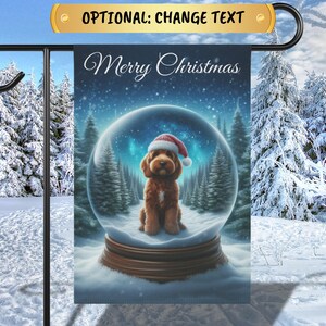 May include: A Christmas-themed garden flag with a brown dog wearing a Santa hat inside a snow globe. The snow globe is surrounded by a snowy forest and the text "Merry Christmas" is at the top of the flag.