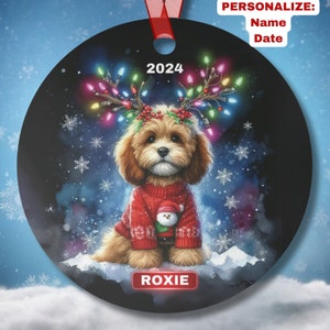 May include: A round Christmas ornament featuring a brown and white dog wearing a red sweater and a reindeer antler headband with colorful lights. The dog is sitting on a snowy background with the year 2024 and the name "ROXIE" printed below.