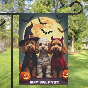 May include: Three dogs dressed in Halloween costumes. A brown dog wearing a witch's hat and black cape, a white dog wrapped in bandages, and a brown dog wearing a red devil costume. The dogs are standing in front of a full moon with bats flying around it. The text "Happy Howl-O-Ween" is at the bottom of the image.