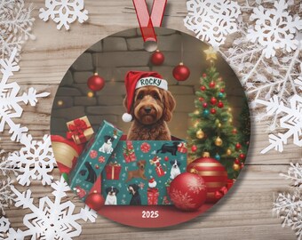 May include: A round Christmas ornament featuring a brown dog wearing a Santa hat with the name "Rocky". The dog is inside a gift box with other dog illustrations. A Christmas tree and ornaments are in the background. The year "2025" is at the bottom.