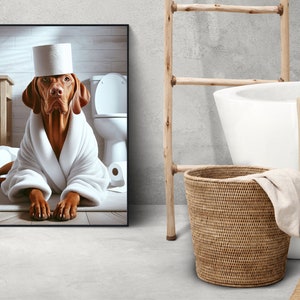 May include: A brown and white dog wearing a white bathrobe and a toilet paper roll hat is sitting on a bathroom floor. The dog is looking at the camera. There is a toilet in the background.